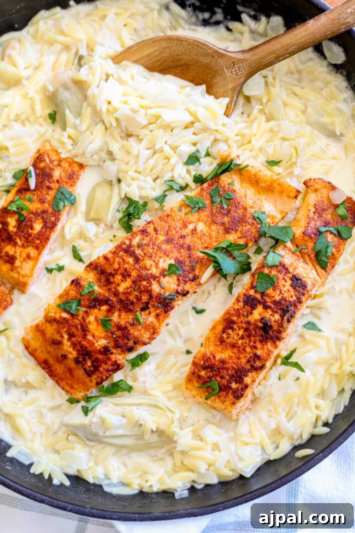 Perfectly cooked salmon fillets served over creamy artichoke orzo, garnished with fresh herbs.