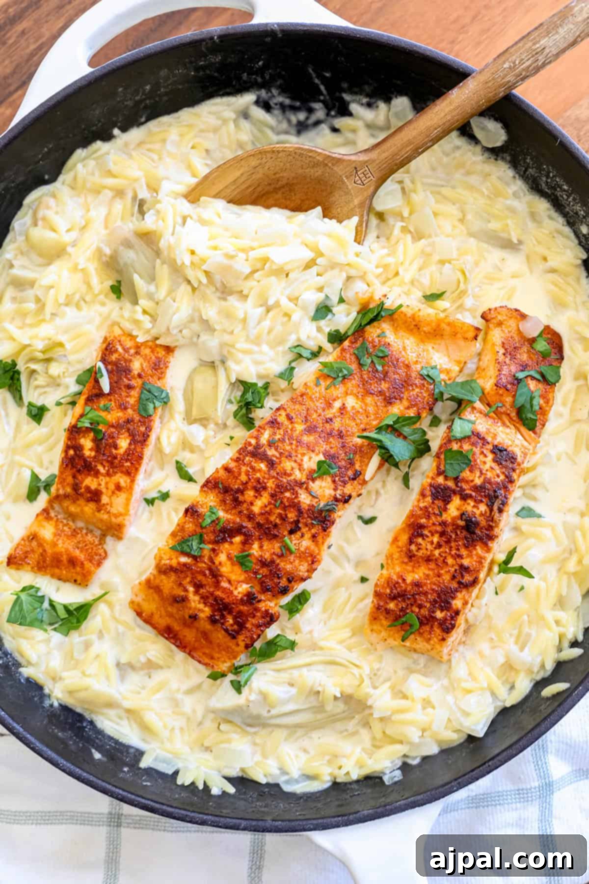 A large skillet filled with creamy artichoke orzo and salmon, ready to be dished out.