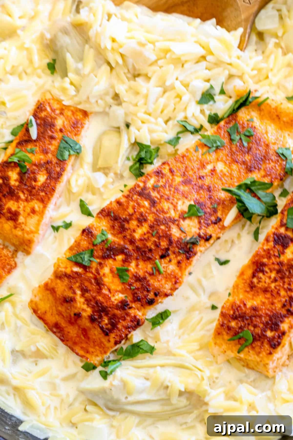 A close-up of a serving of salmon with artichoke orzo in a white bowl, garnished with fresh herbs.