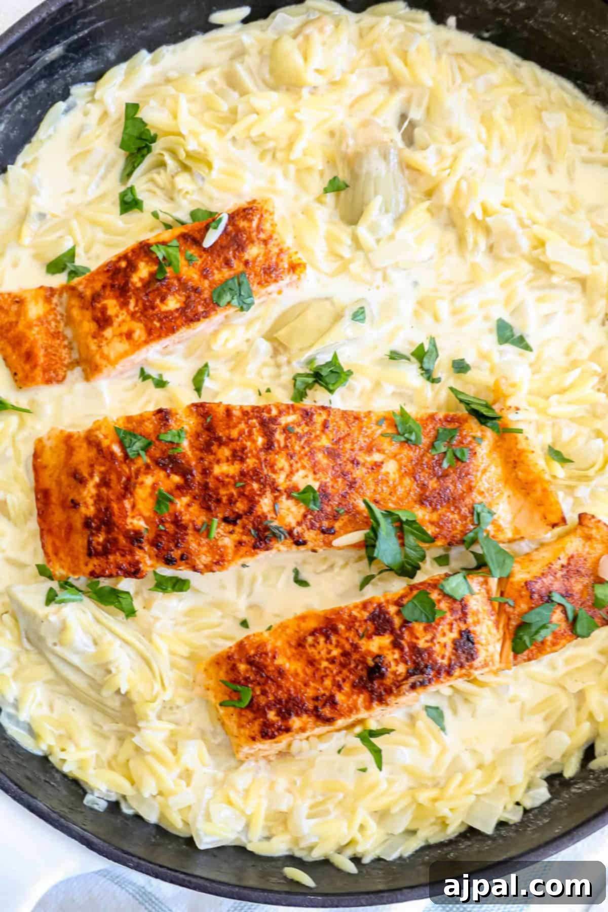 A serving of creamy salmon with artichoke orzo, garnished with chili flakes and parsley.