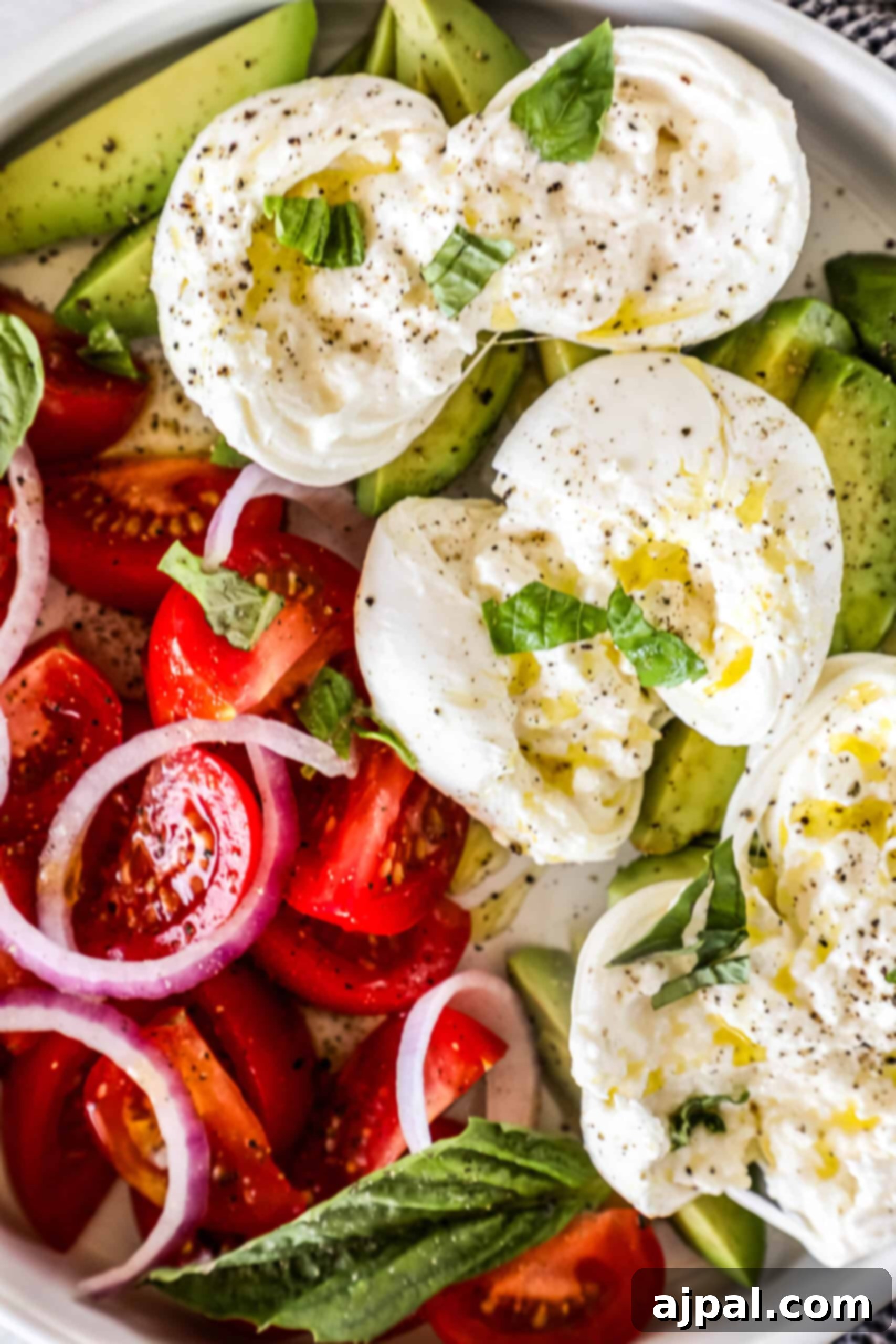 Creamy Burrata Avocado Tomato Salad 4 A close-up shot of a single ball of burrata cheese, perfectly round and white, sitting on a bed of vibrant red tomatoes and green avocado slices, adorned with fresh basil leaves.