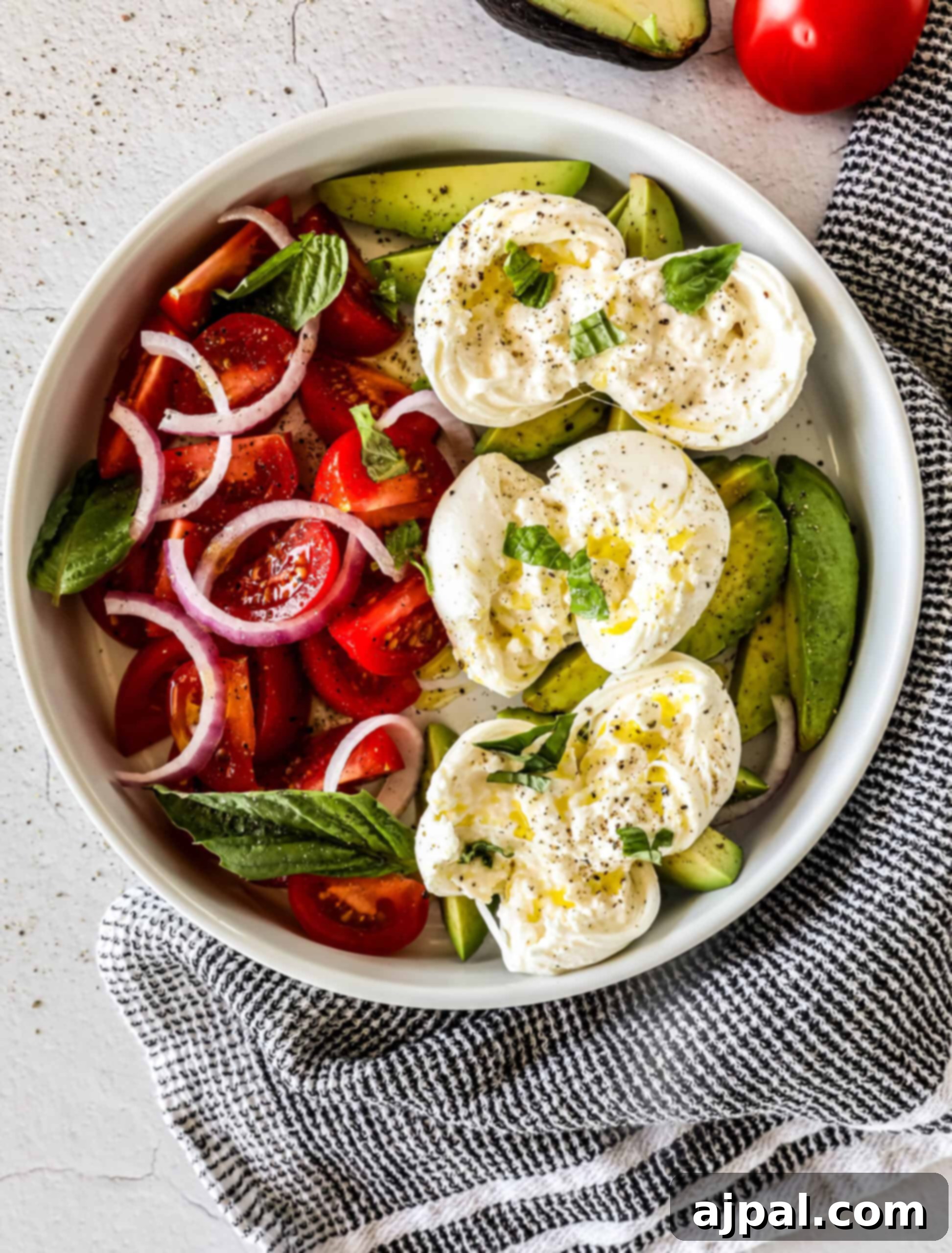 Creamy Burrata Avocado Tomato Salad 5 Two serving bowls of Burrata Tomato and Avocado Salad, each portion featuring a half burrata ball, sliced tomatoes, avocado, and red onion, garnished with fresh basil.