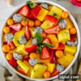 A bowl filled with a colorful tropical fruit salad consisting of sliced strawberries, pineapple, mango, dragon fruit, and golden berries, garnished with fresh mint leaves.