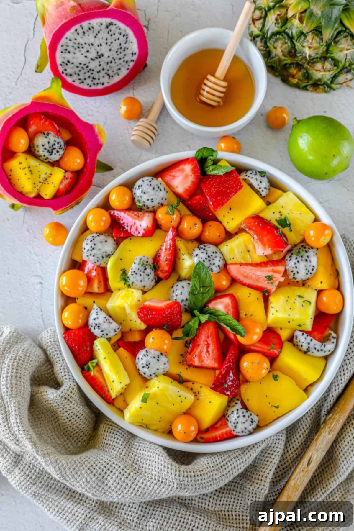 Paradise Fruit Medley 3 A close-up shot of the colorful tropical fruit salad in a white bowl, showcasing the vibrant reds of strawberries, yellow pineapple, orange mango, and white dragon fruit, with green mint leaves.