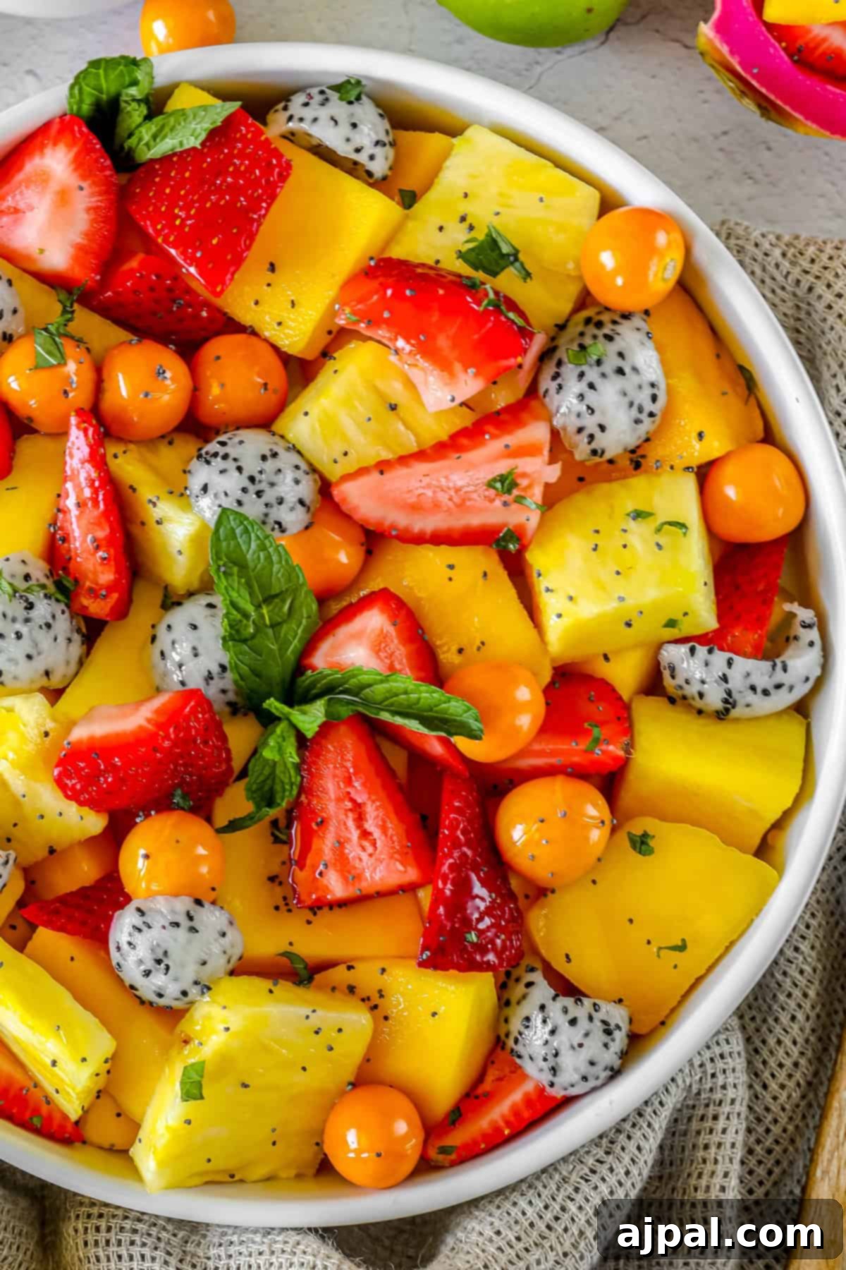 Paradise Fruit Medley 4 A vibrant tropical fruit salad with generous slices of mango, golden berries, dragon fruit, and pineapple, glistening with dressing and garnished with fresh mint.