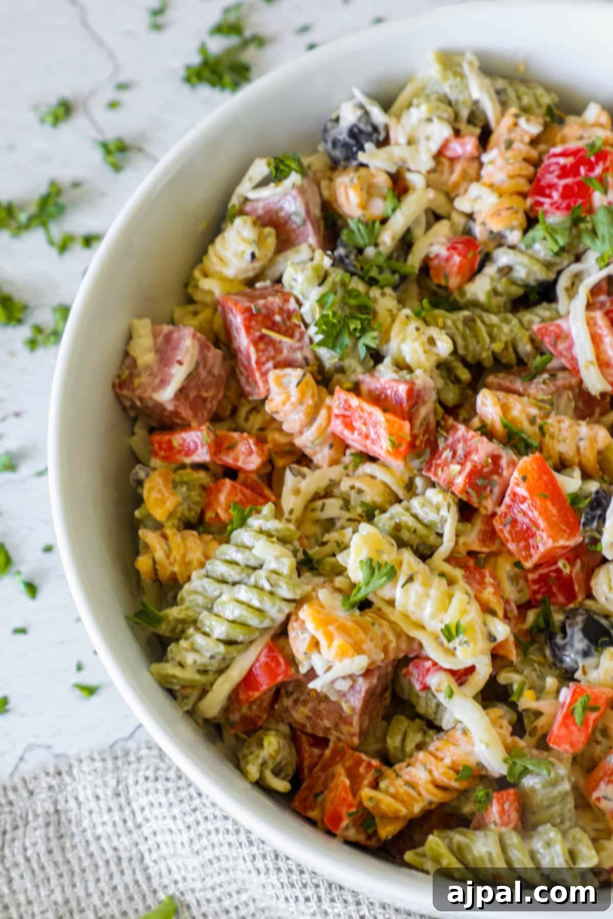 Creamy Italian Pasta Salad 2 A vibrant bowl of creamy Italian pasta salad featuring spiral rotini pasta, diced red bell peppers, black olives, mozzarella cubes, and fresh herbs, ready to be served.