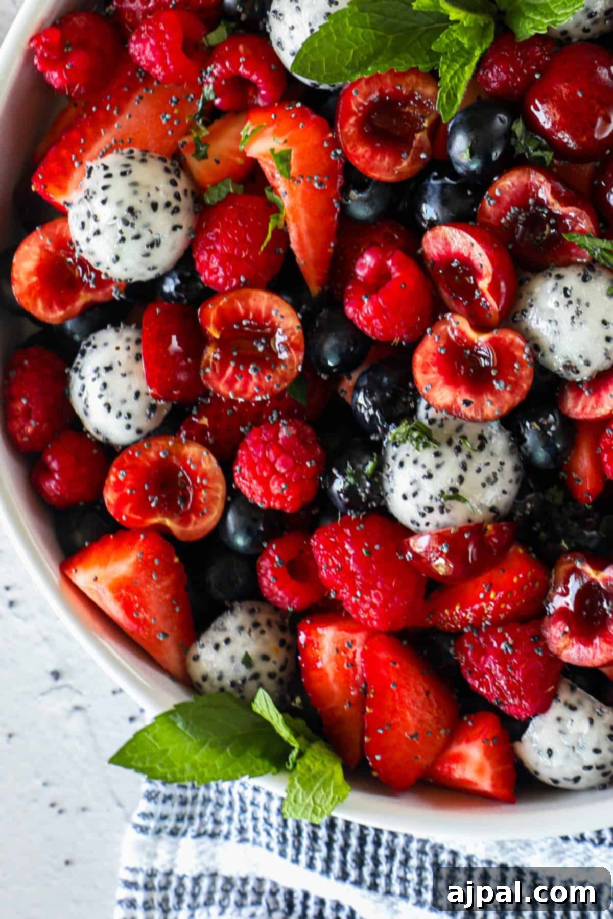 Sweet Berry Burst 4 A bowl of mixed fruit salad containing strawberries, raspberries, blueberries, cherries, dragon fruit balls, and garnished with fresh mint leaves, showcasing the vibrant colors of a summer fruit salad.