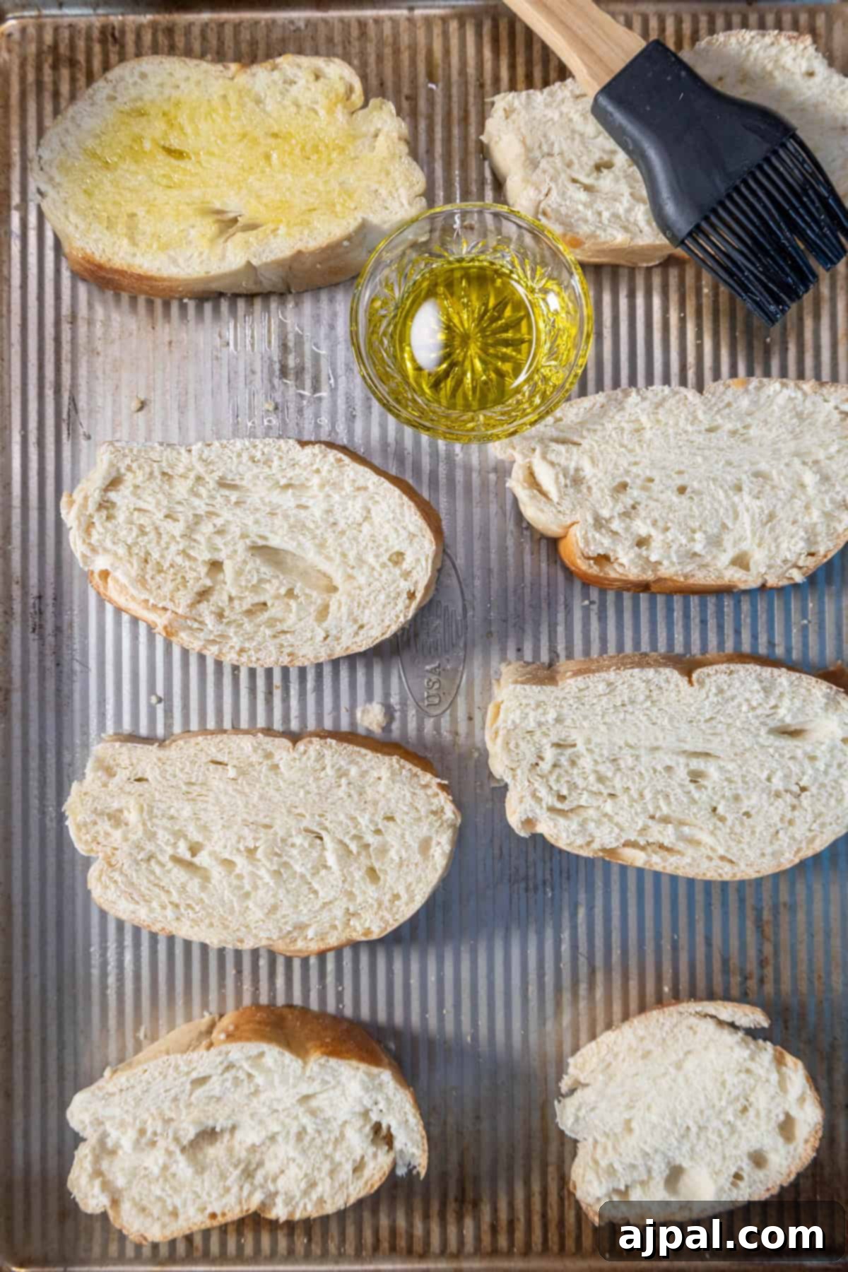 Bread slices generously drizzled with olive oil on a baking sheet, ready for the oven.