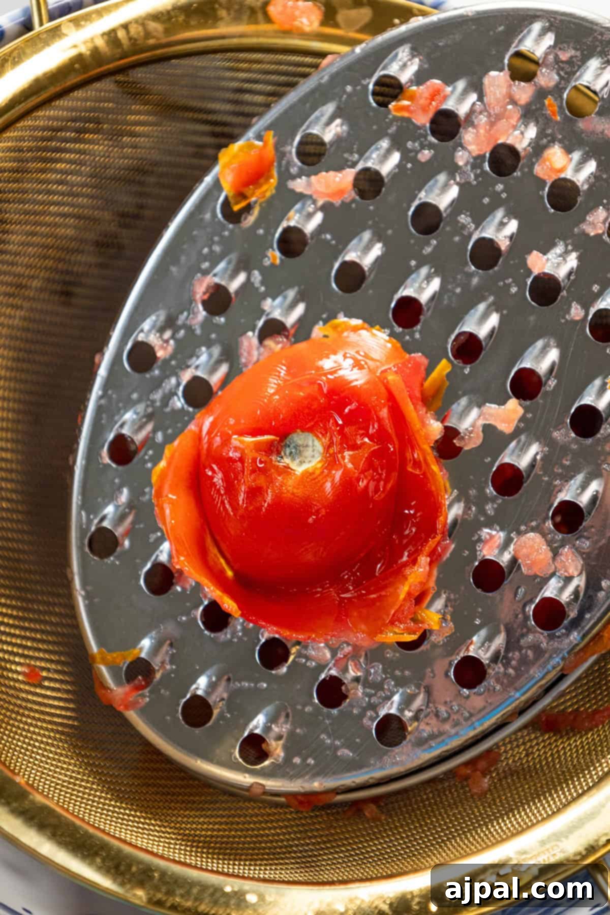 The process of grating fresh, ripe tomatoes over a mesh strainer, preparing them for Pan Con Tomate.
