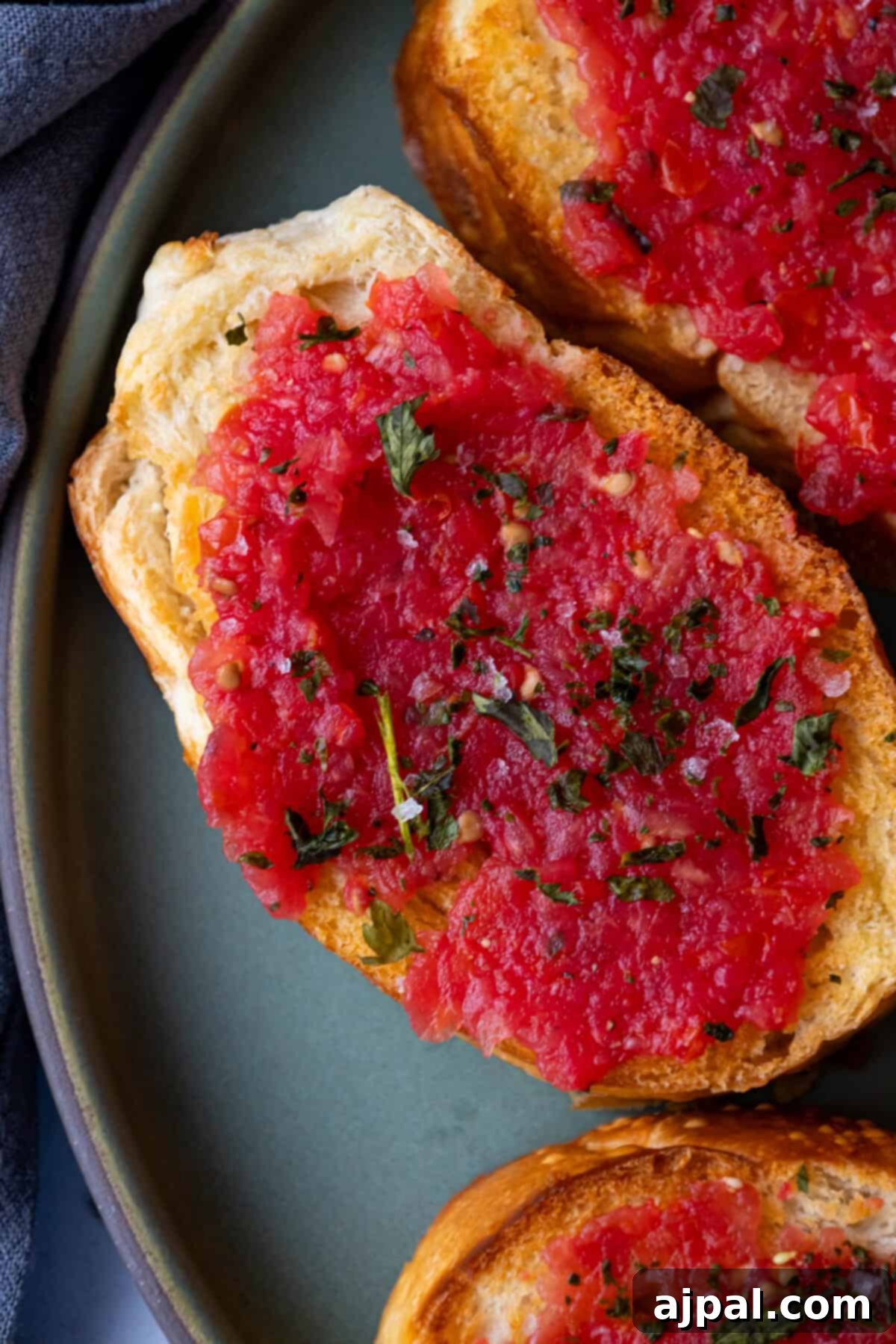 A vibrant close-up of Spanish Tomato Bread (Pan con Tomate) on a cutting board, highlighting the fresh tomato and olive oil.