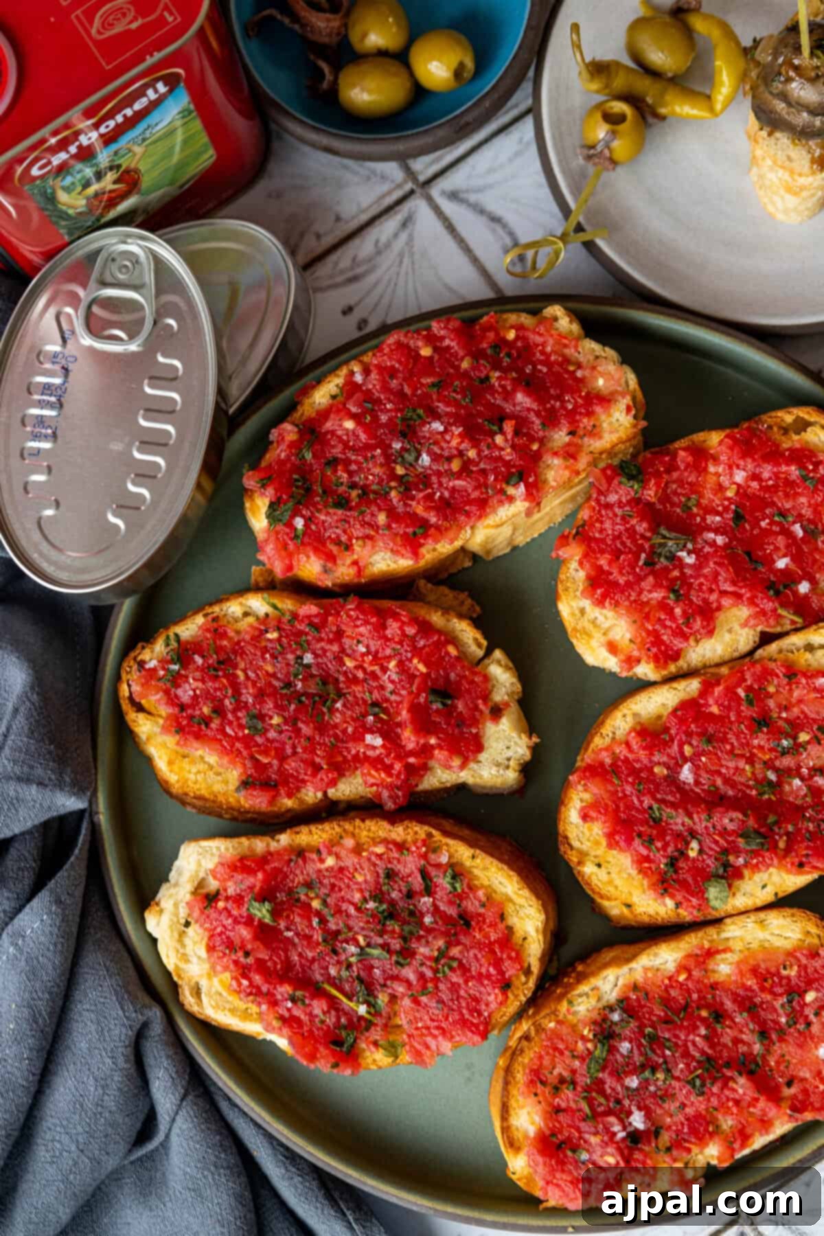 Close-up of Spanish Tomato Bread (Pan Con Tomate) with vibrant red tomatoes and green herbs.