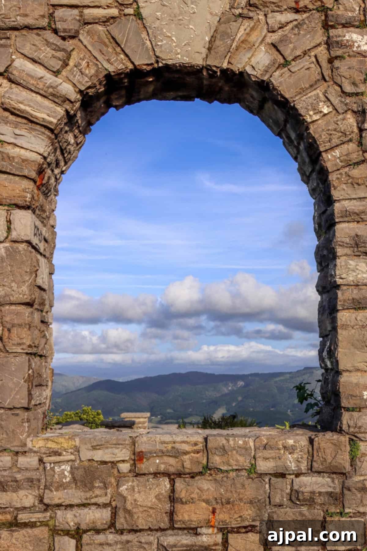 Hondarribia Uncovered 10 A stone arch window frame reveals a scenic view of mountains under a blue sky with scattered clouds.