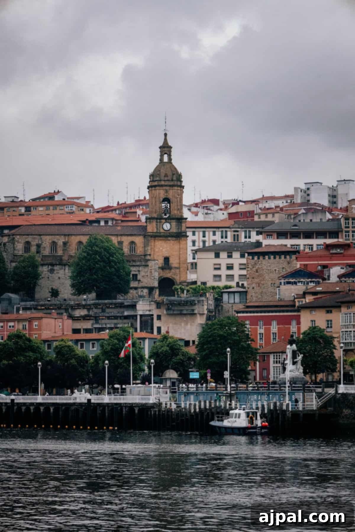 A charming waterfront scene in Bilbao, showcasing historic buildings, a clock tower, and boats gently docked on the Nervión River.