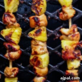 Pineapple Chicken Kebabs sizzle on the grill, their char marks enhancing the succulent chicken pieces and juicy pineapple chunks.