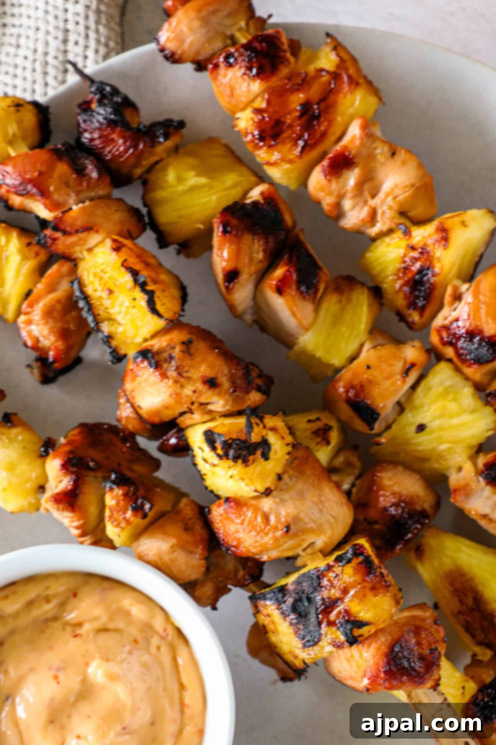 Tropical Chicken & Pineapple Skewers 4 Close-up of grilled pineapple chicken kebabs served on a platter with a side of rich, reduced marinade sauce.