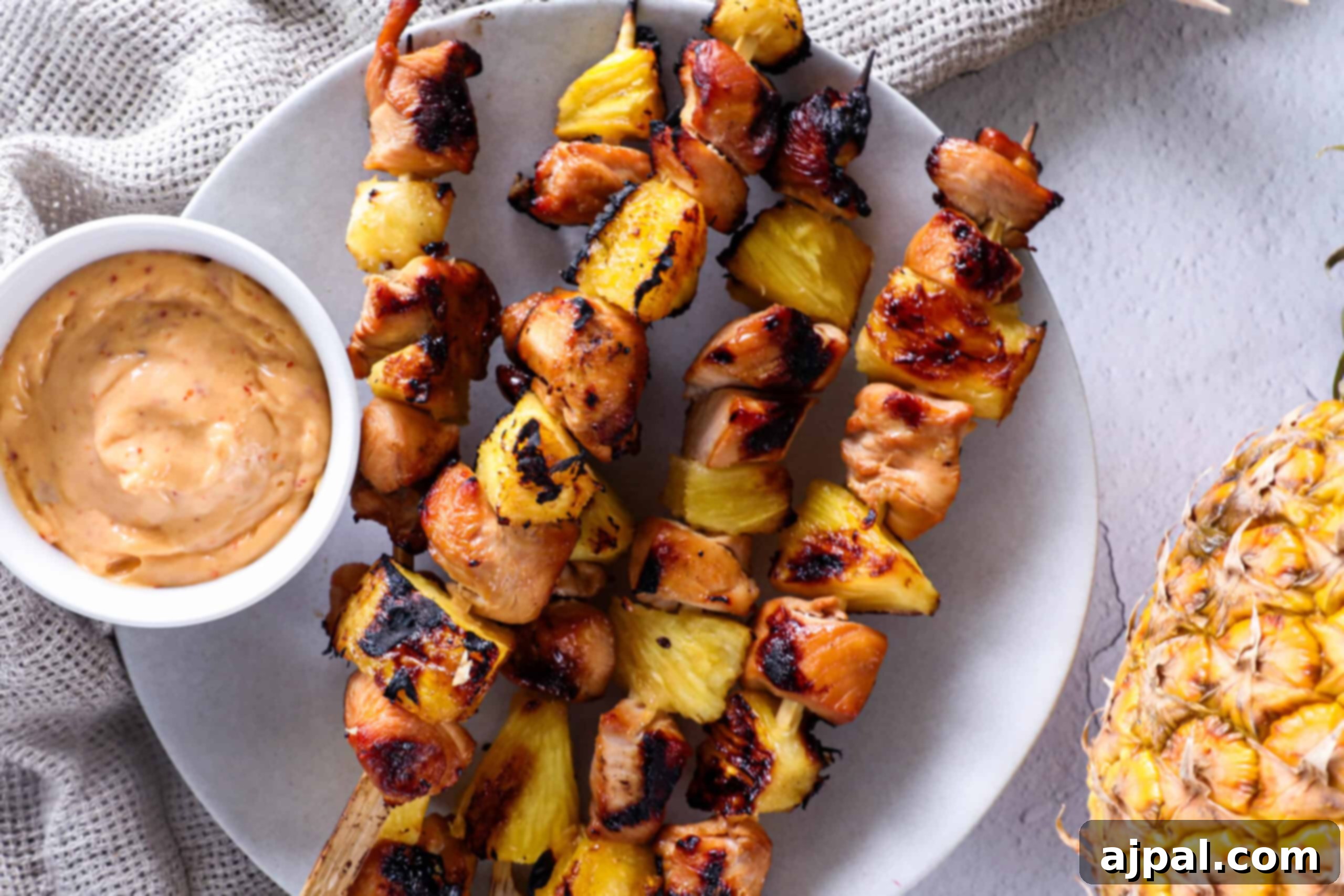 Tropical Chicken & Pineapple Skewers 5 Beautifully arranged grilled pineapple and chicken skewers on a serving platter, with a small bowl of dipping sauce.
