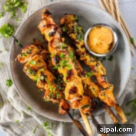 Dynamite Bang Bang Chicken Skewers 8 A plate with grilled chicken skewers garnished with herbs, accompanied by a small dish of dipping sauce.
