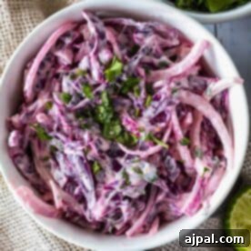 A bowl of creamy coleslaw made with purple cabbage and garnished with chopped herbs.