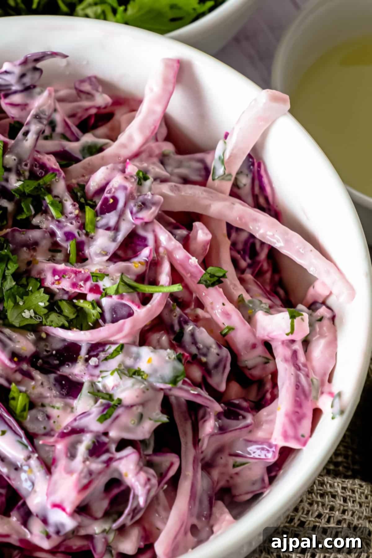 Simple Taco Slaw 8 A close-up of a white bowl filled with vibrant purple coleslaw, garnished with chopped green herbs and mixed with a creamy dressing.