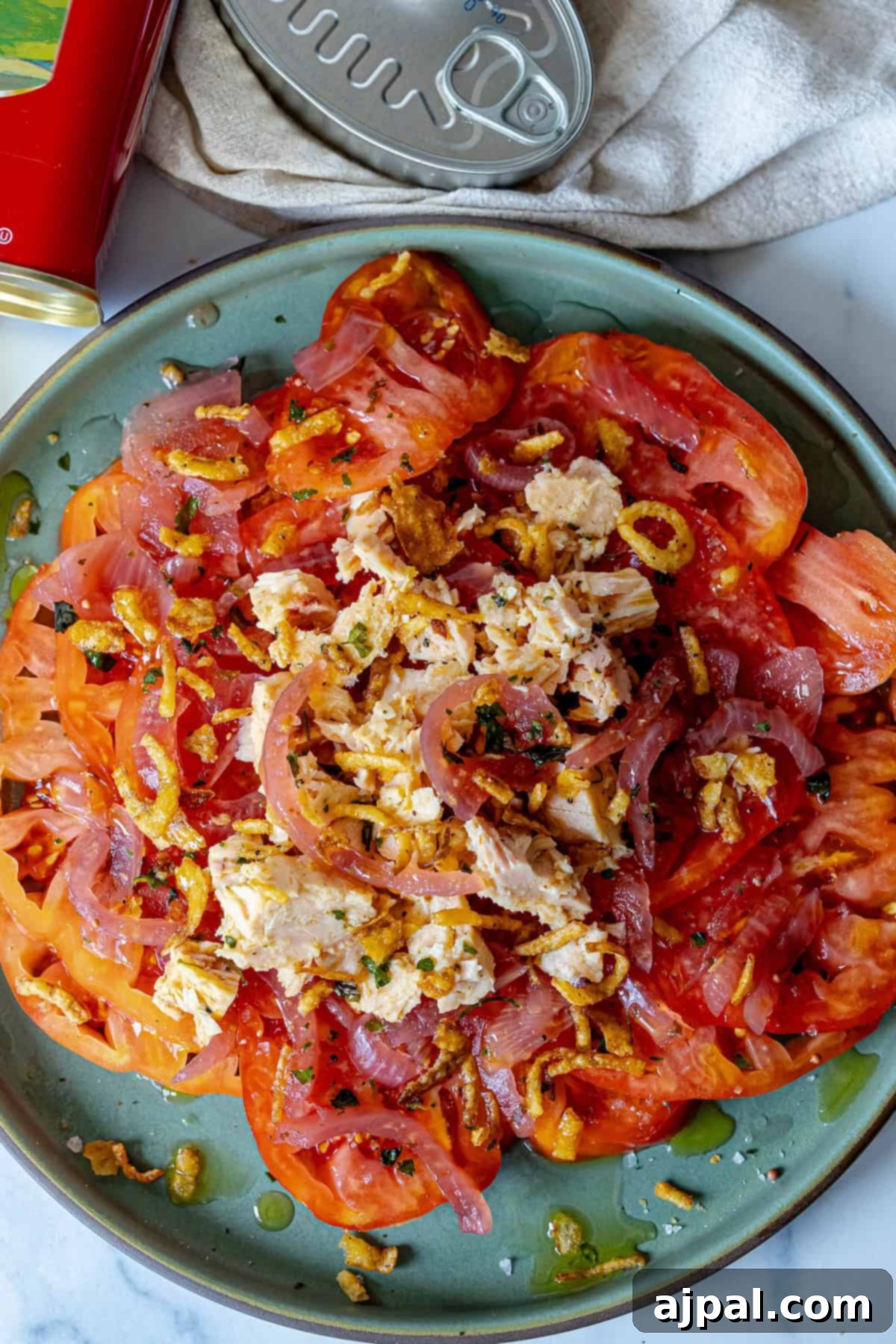 A serving of Spanish tuna and tomato salad, glistening with olive oil and topped with crispy fried onions.