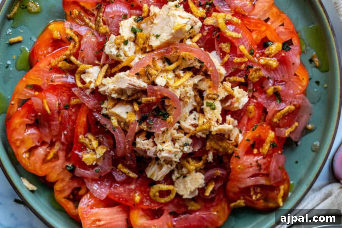 Overhead view of a prepared tuna and tomato salad on a rustic wooden table, garnished with fresh herbs.