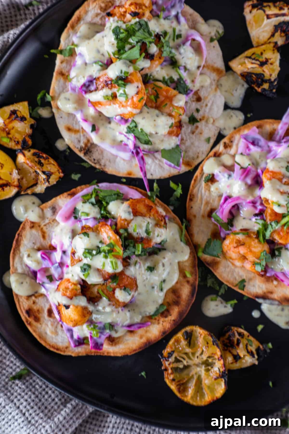 Coastal Shrimp Tacos 7 Three grilled shrimp tacos topped with creamy sauce, shredded purple cabbage, and cilantro, artfully arranged on a black plate with grilled lime wedges on the side.