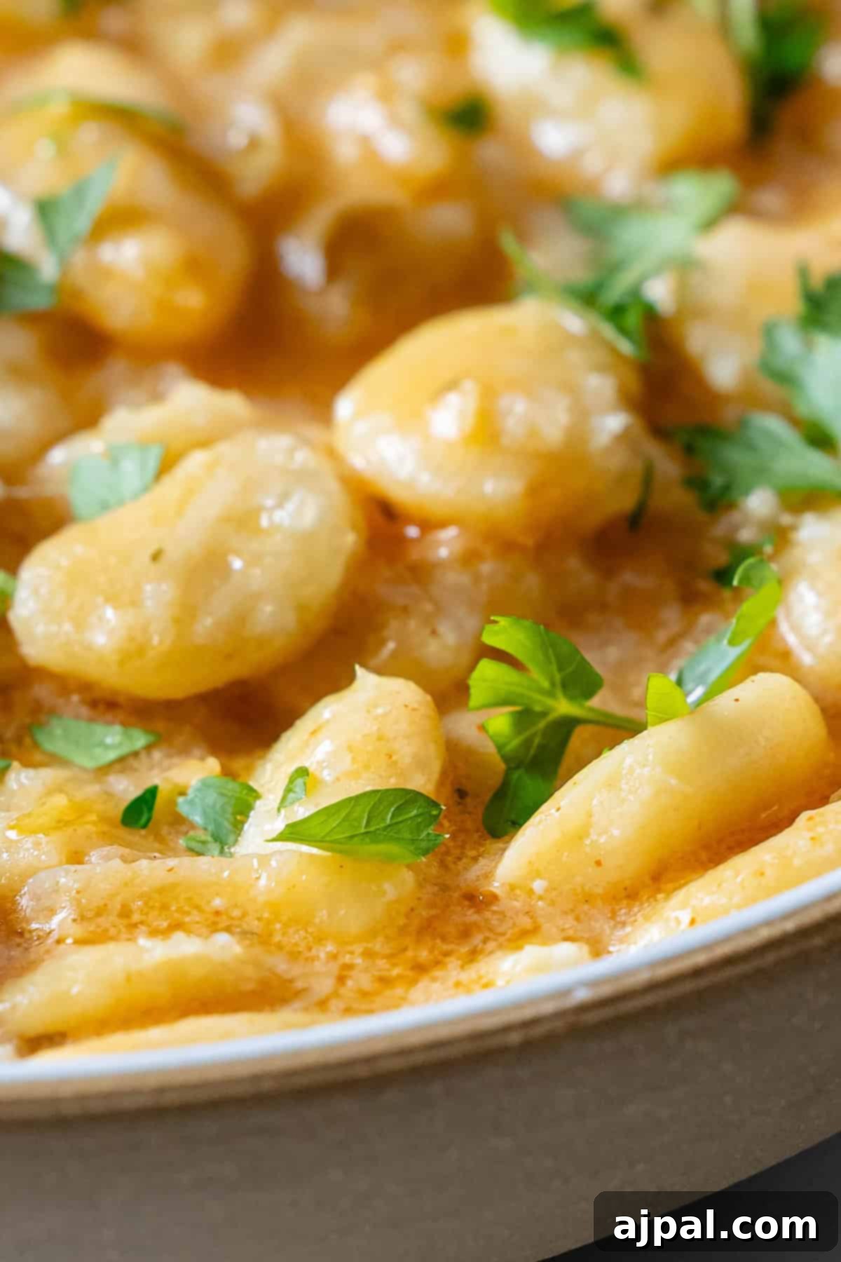Velvety Garlic Butter Beans 5 A vibrant bowl of creamy garlic chili butter beans, beautifully styled with fresh herbs and whole red chilies on top.