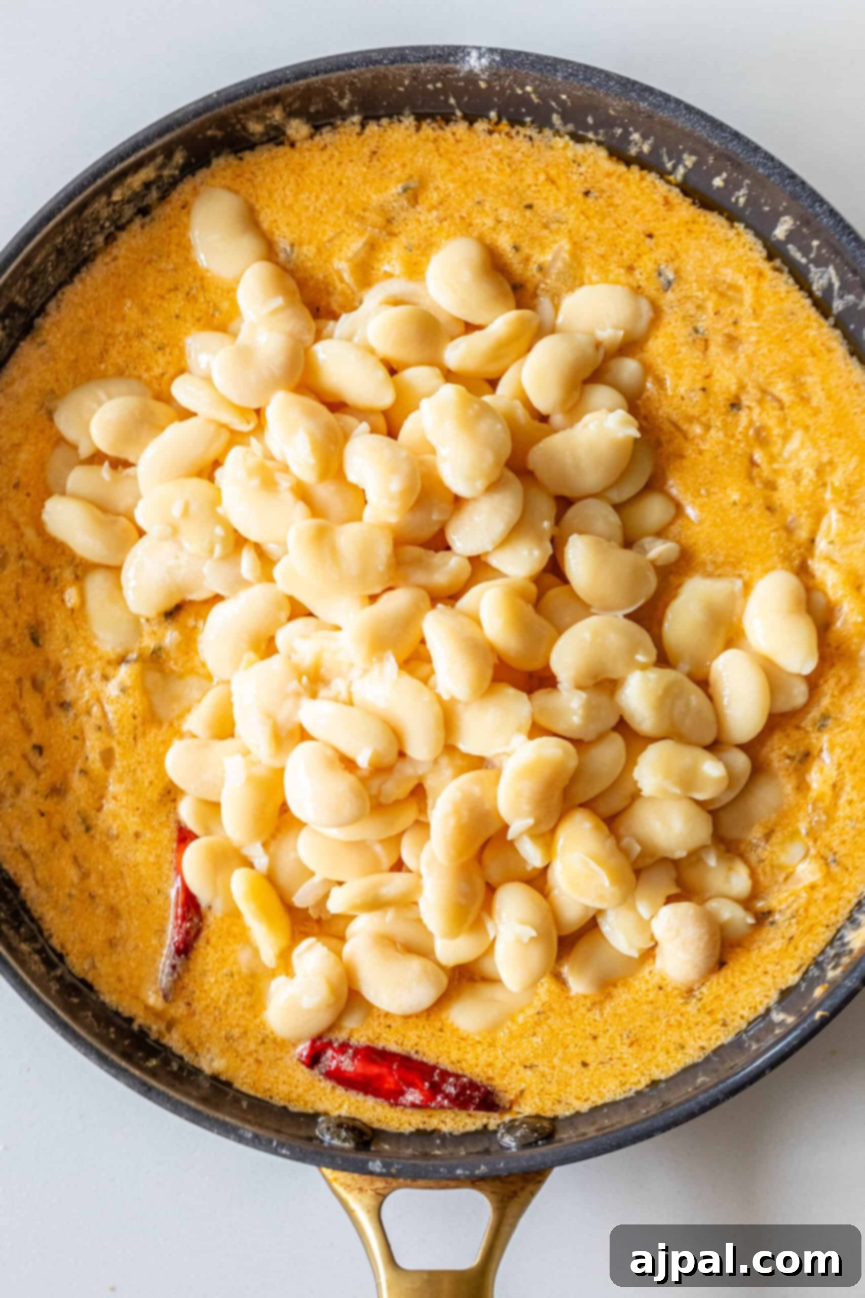 Velvety Garlic Butter Beans 8 Butter beans being stirred into the simmering creamy garlic chili sauce in a pan.