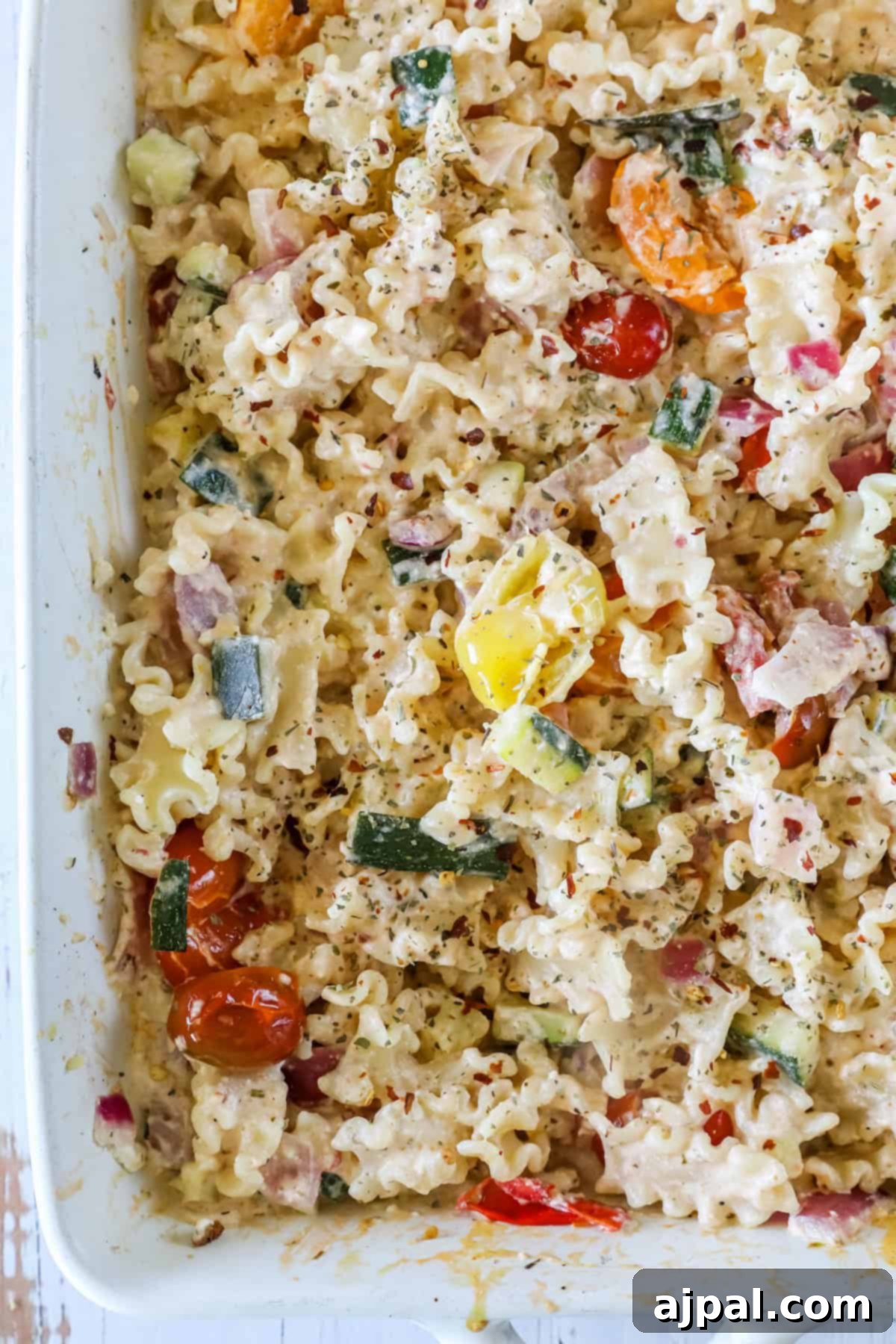 Baked Feta Pasta Bliss 4 A close-up view of a pasta salad with mafaldine noodles, cherry tomatoes, zucchini, red onion, and a creamy dressing in a white dish.