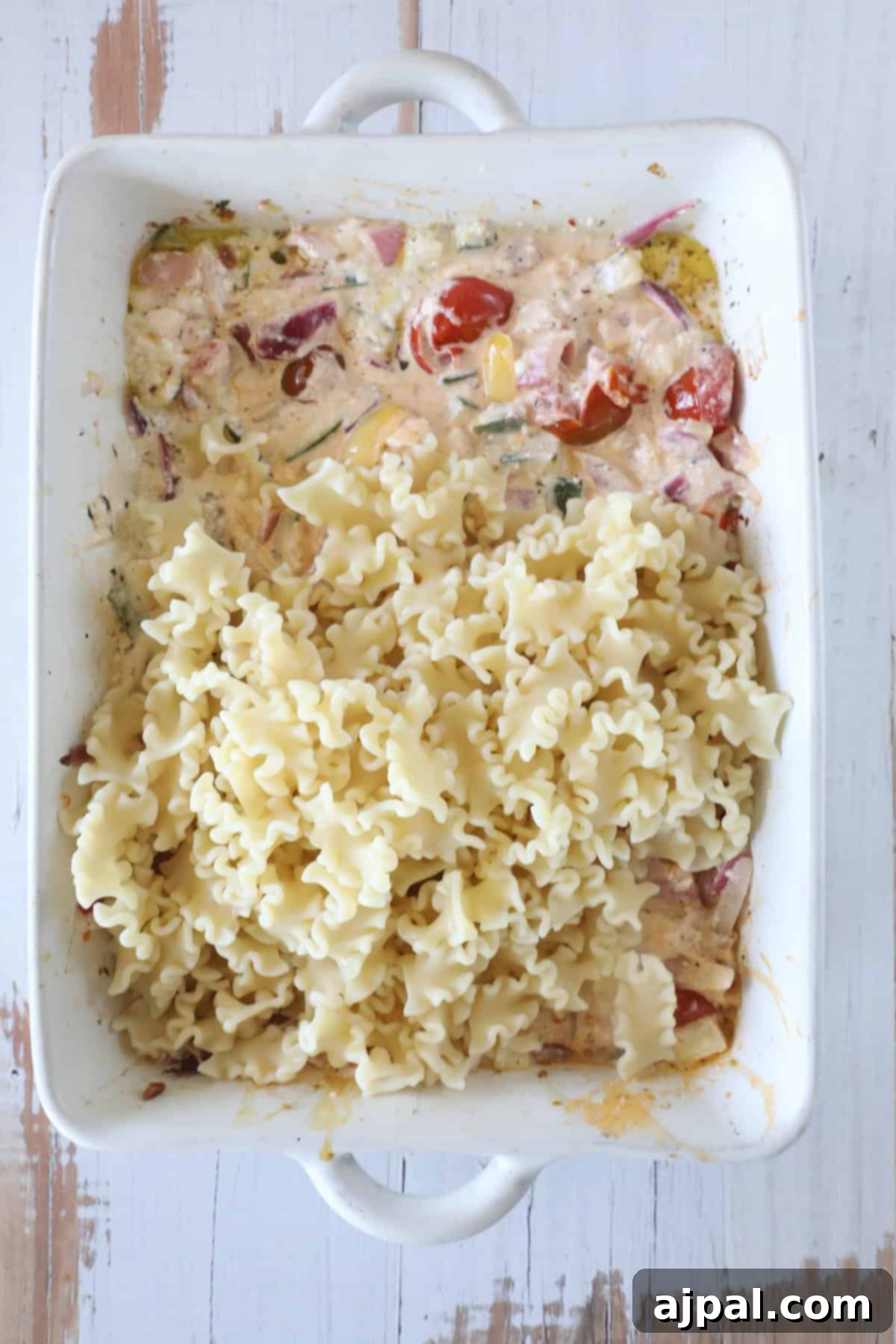 Baked Feta Pasta Bliss 8 A white baking dish filled with cooked pasta on one side and a creamy mixture with cherry tomatoes, onions, and spices on the other side.
