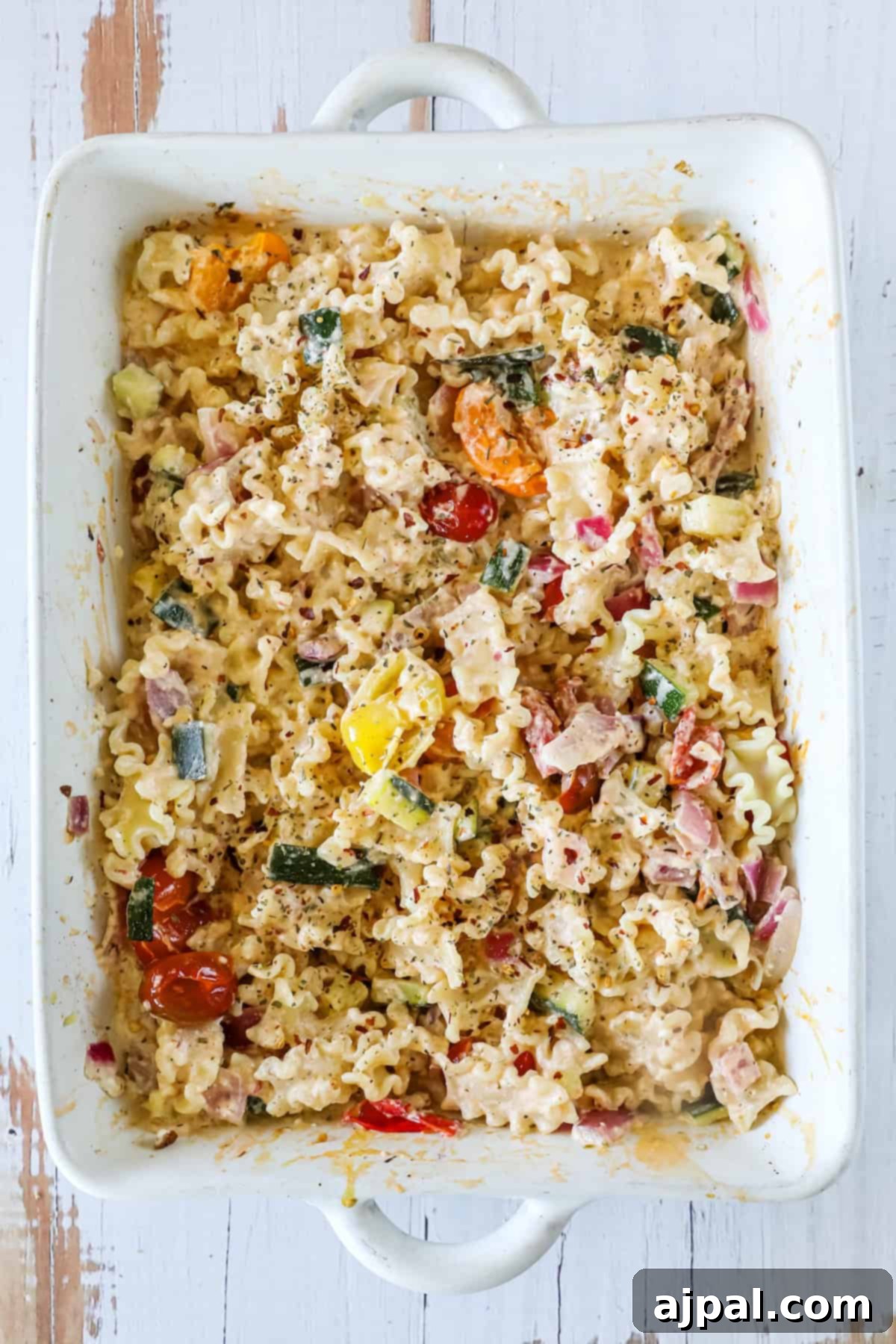 Baked Feta Pasta Bliss 10 A rectangular casserole dish filled with cooked pasta, tomatoes, zucchini, and herbs mixed with a creamy sauce.