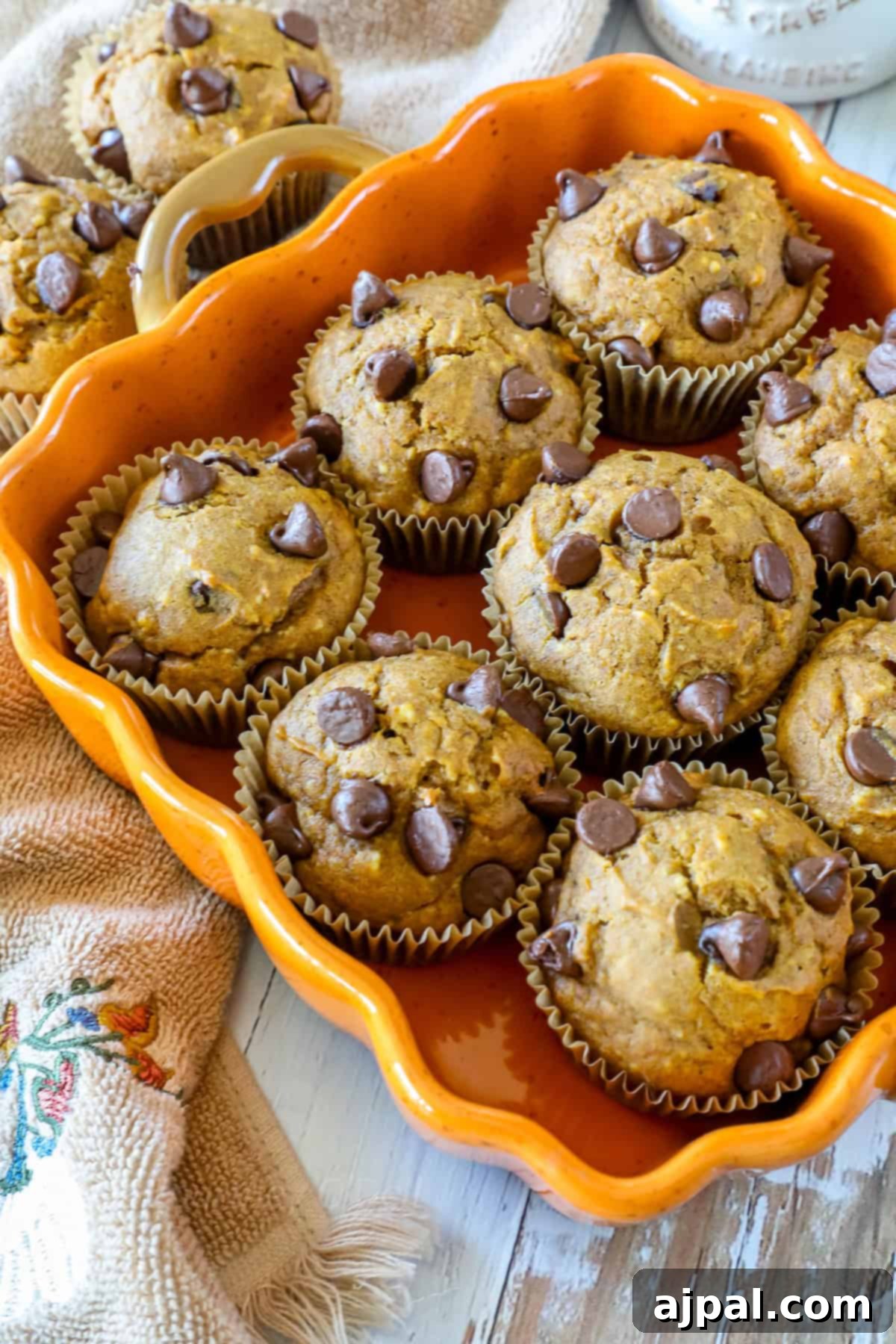 Orange tray filled with chocolate chip muffins, surrounded by a beige cloth on a wooden surface.