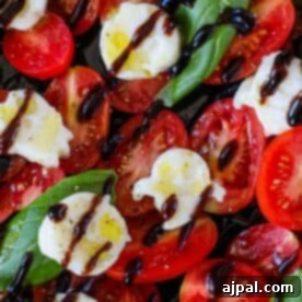 A close-up of a Spooky Caprese Salad with sliced tomatoes, mozzarella shaped into ghosts and skulls, fresh basil leaves, and balsamic glaze drizzled on top. This image highlights the festive presentation.