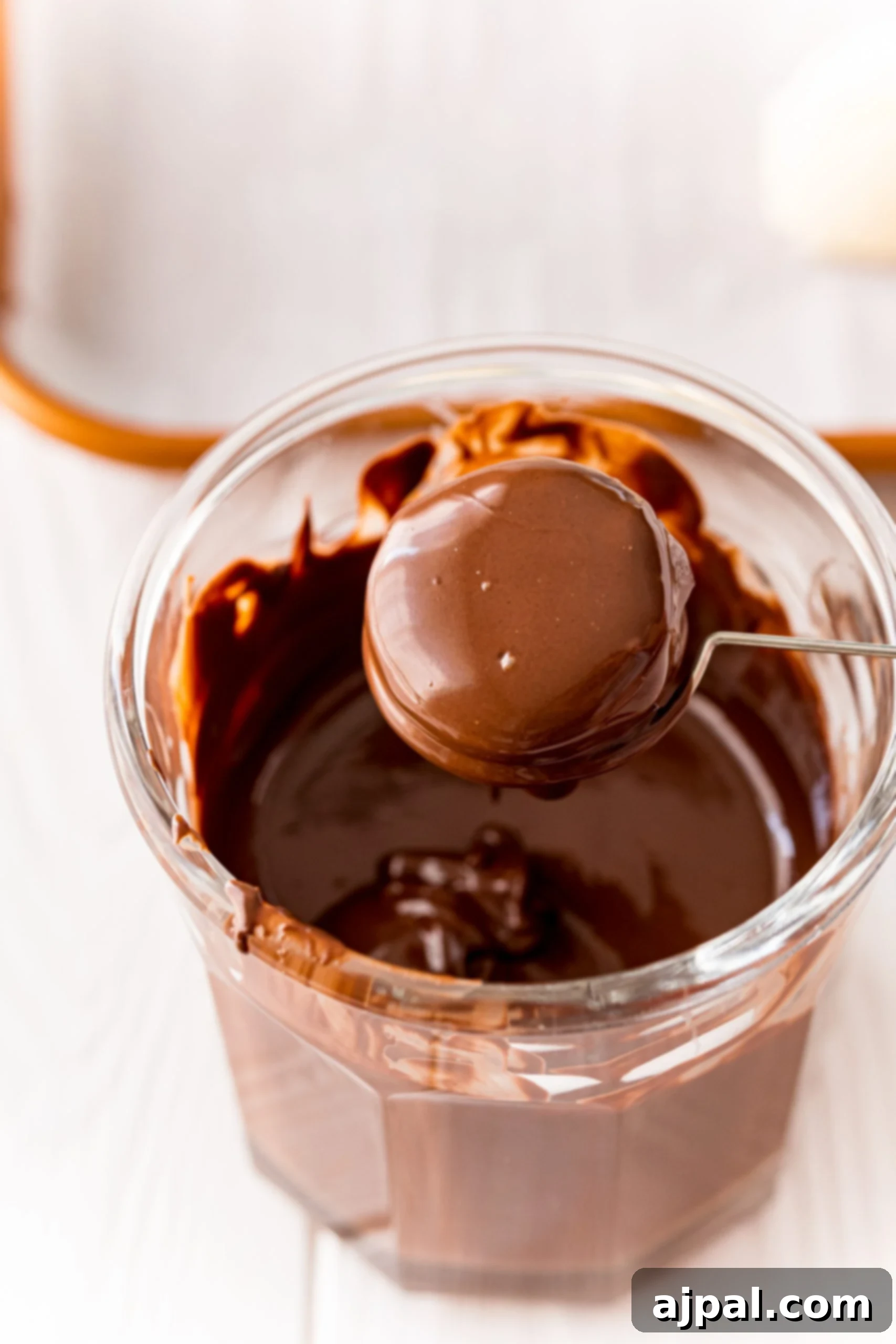 A bowl of chocolate ganache with a spoon and butter cream truffles on top.