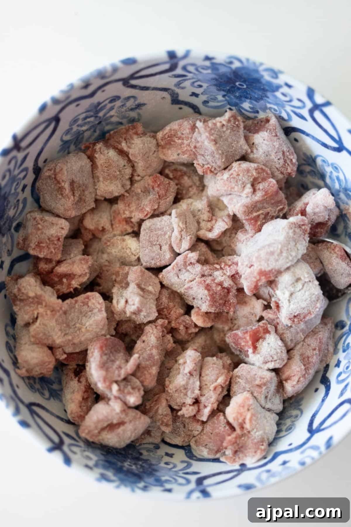 Simple Beef Stew 6 Chunks of raw meat coated in flour sit in a blue and white patterned bowl, ready to become a classic beef stew.