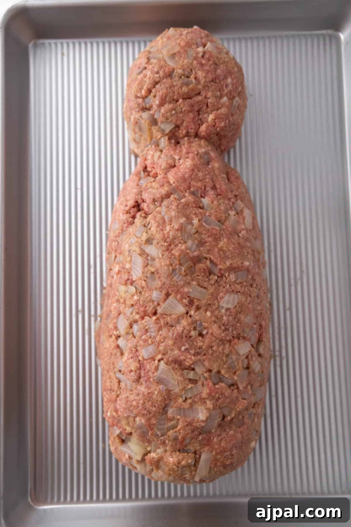 Ground meat mixed with diced onions, shaped roughly like a mummy on a metal baking tray, ready for baking.