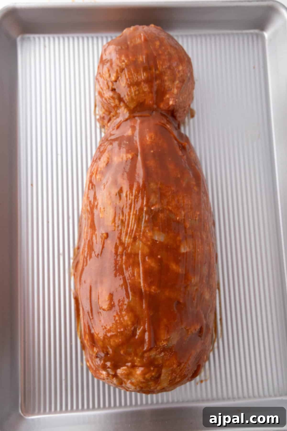 A large mummy meatloaf covered in a rich sauce, resting on a ribbed baking sheet.