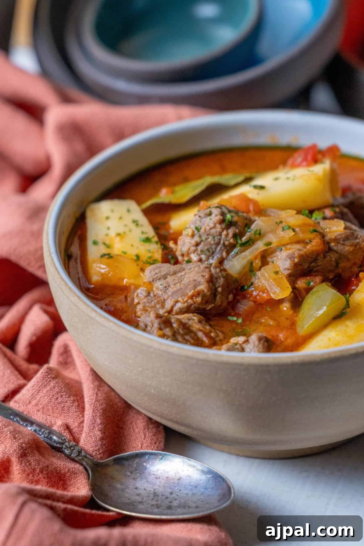 A comforting bowl of hearty beef stew with tender potatoes, onions, and herbs, invitingly placed on a table adorned with an orange cloth. A spoon rests nearby, ready to enjoy the savory medley, enriched by the addition of parsnips.