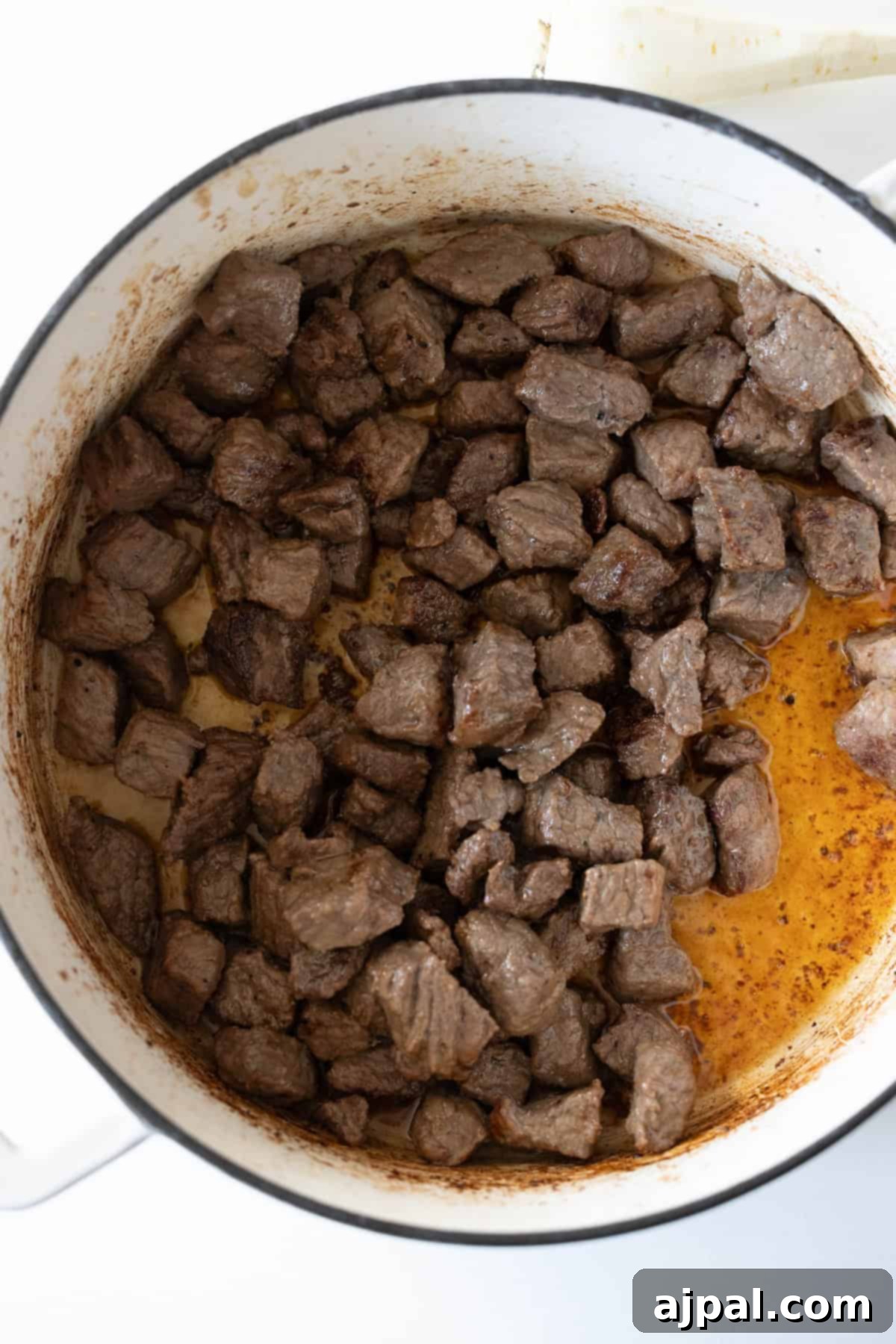 Cooked beef cubes in a white pot, displaying beautifully browned edges and rich, savory cooking juices at the bottom—an excellent foundation for a hearty beef stew.