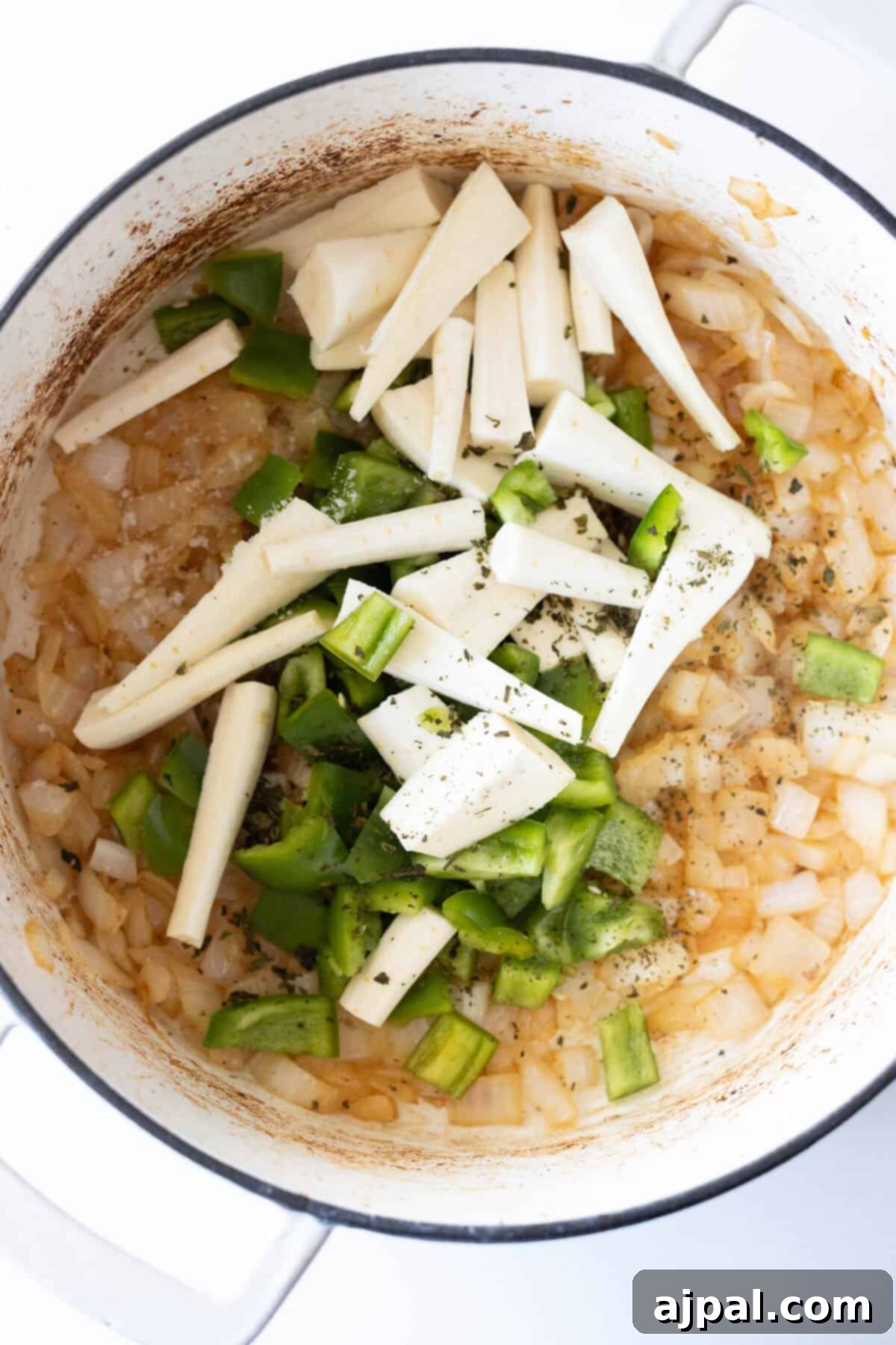 Chopped onions, vibrant green bell peppers, and sweet parsnips are simmering together in a pot, creating a savory and aromatic blend for the beef stew.