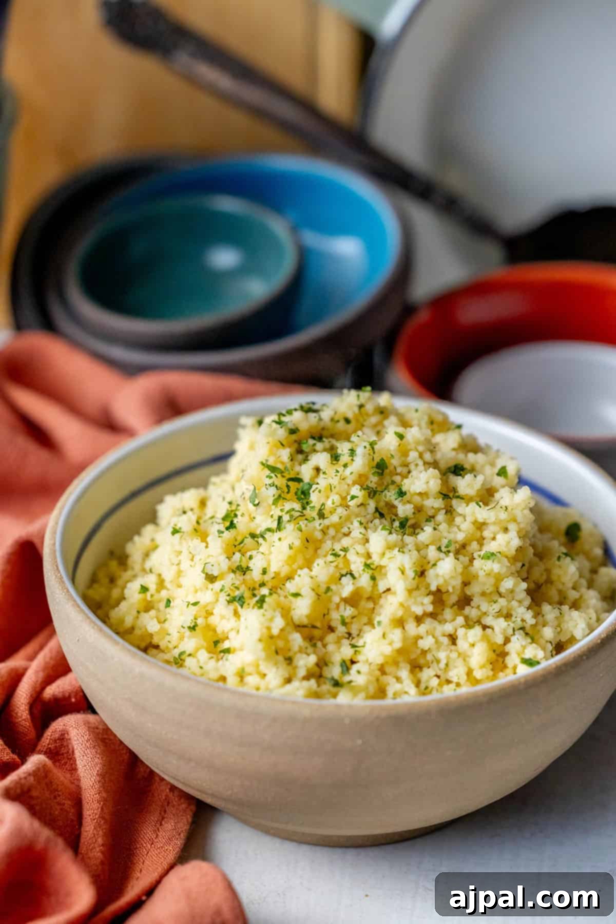 Authentic Couscous Delights 3 A bowl of fluffy couscous, crafted from a simple recipe and garnished with herbs, sits elegantly on a table, surrounded by stacked bowls and an orange napkin.