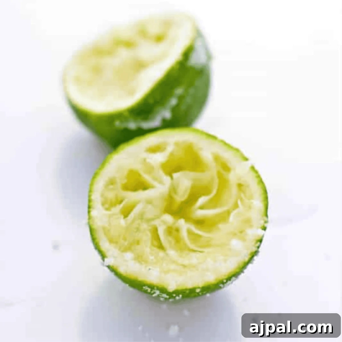 Tequila's Zesty Salted Kiss 4 Two halves of a squeezed lime are shown on a white surface, with some lime pulp and juice visible, perfect for your Salted Lime Tequila Shooters.