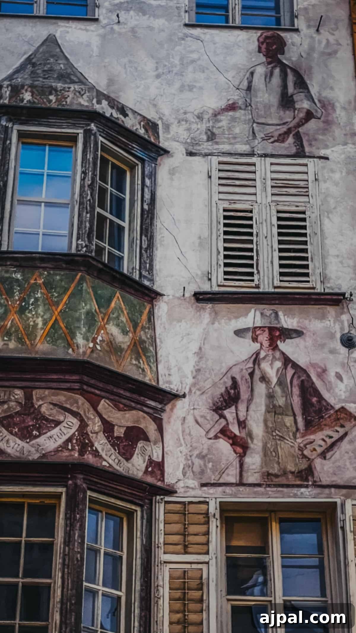 Bolzano's Magical Christmas Market 13 The facade of an old building in Bolzano features murals depicting human figures, decorative patterns, and multiple windows with shutters, reminiscent of a Christmas market's charm.
