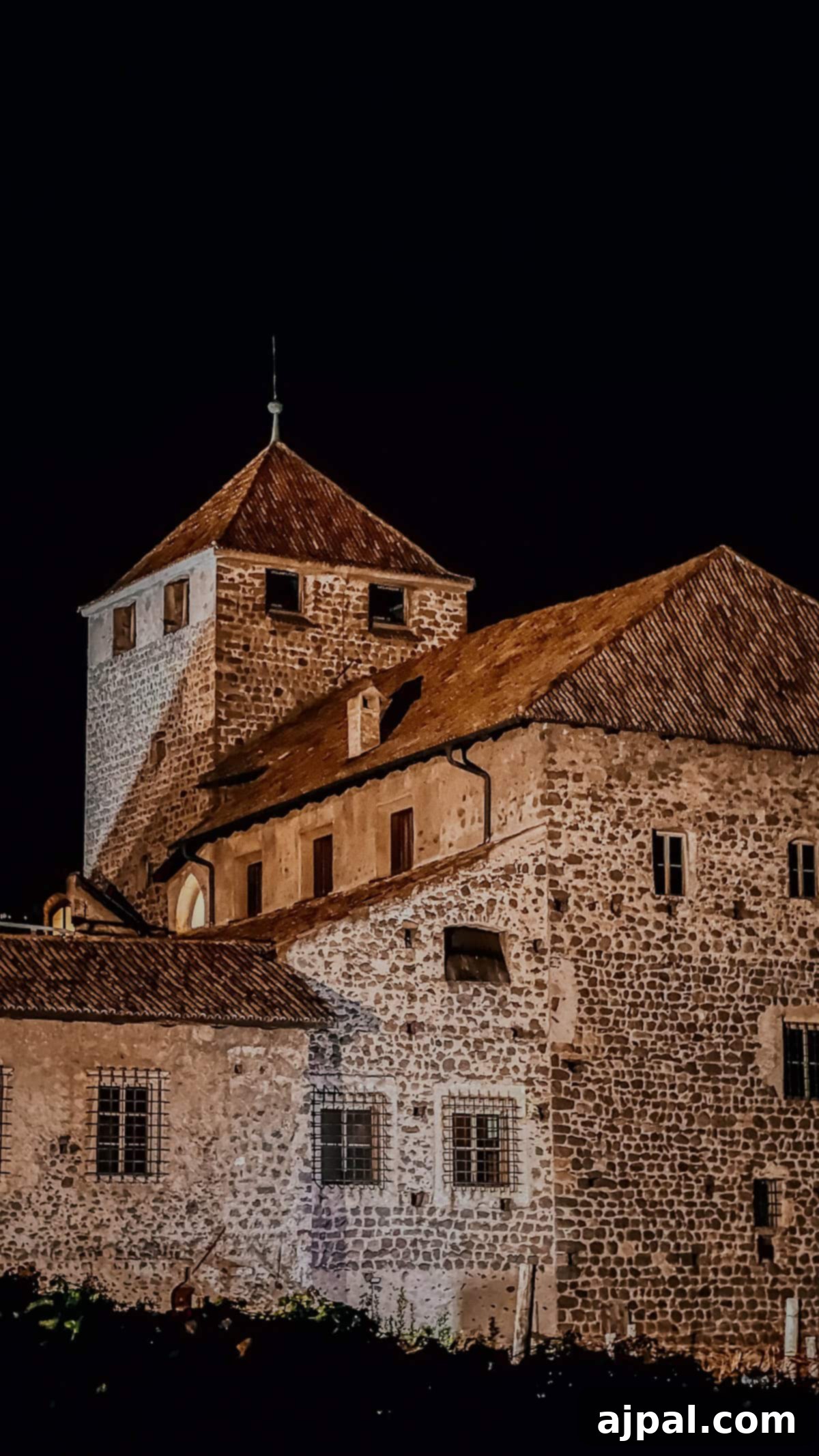 Bolzano's Magical Christmas Market 14 Night view of a stone building with a tower, featuring a triangular roof and small windows, reminiscent of Bolzano's charm during Christmas, set against a dark sky.