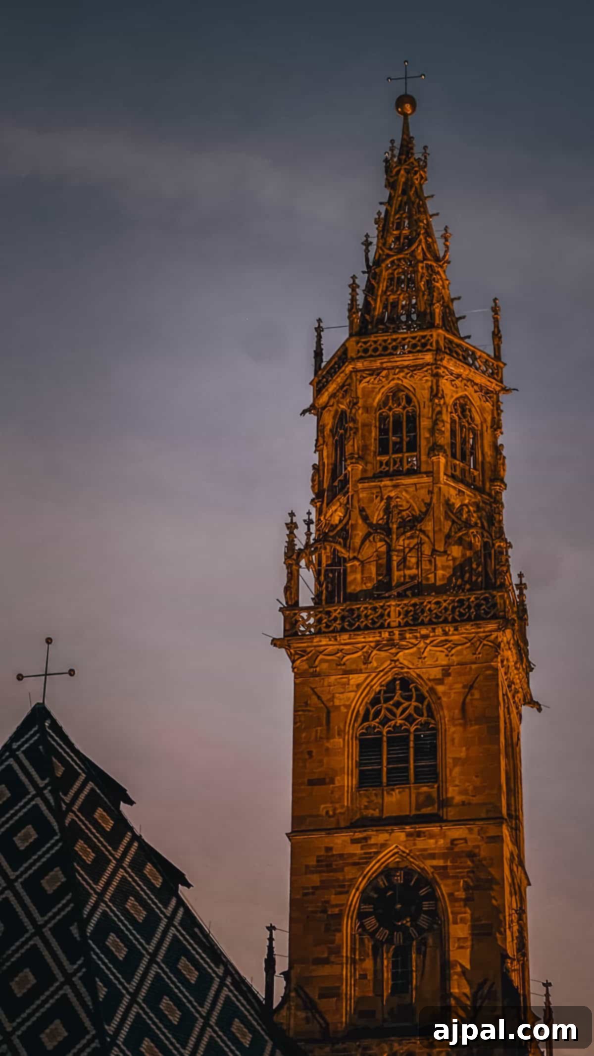 Bolzano's Magical Christmas Market 15 Against a dusky sky, the tall gothic-style church tower in Bolzano stands with detailed stone carvings and a clock, overlooking the festive Christmas market below.