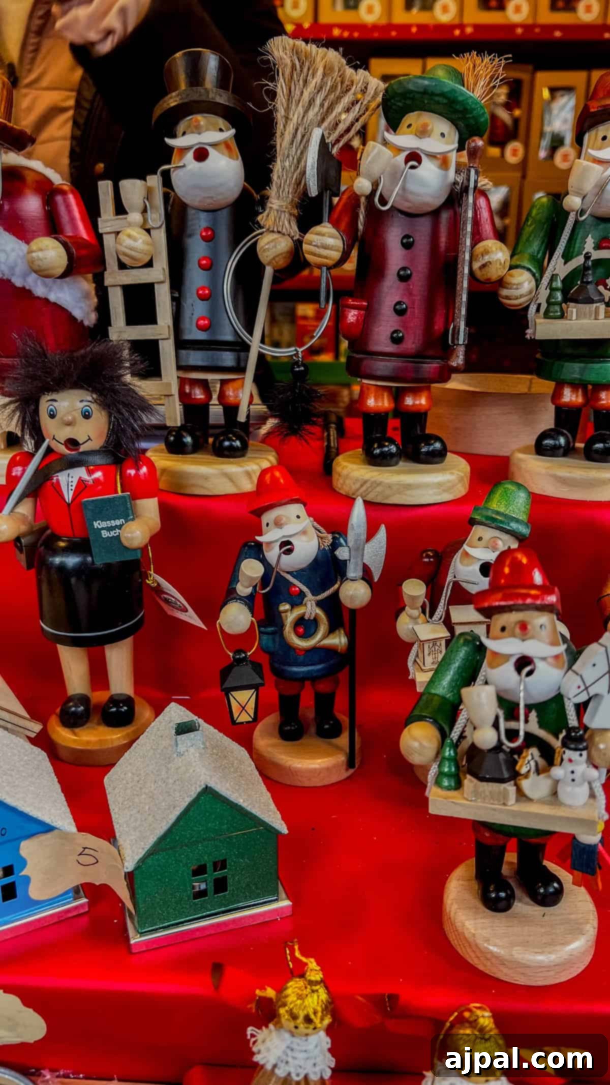 Bolzano's Magical Christmas Market 6 A festive display features wooden nutcracker figures in various costumes, arranged on a red surface. In front, small green and gray model houses evoke the charm of Bolzano's Christmas market.