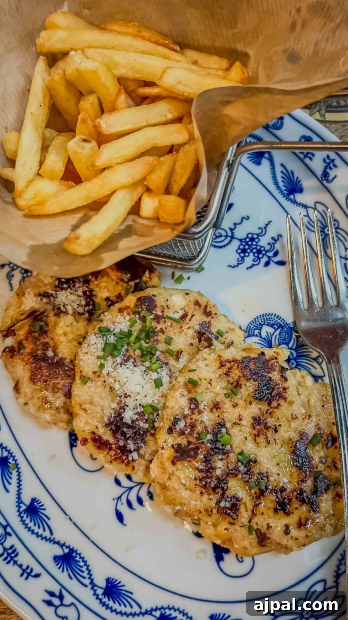 Bolzano's Magical Christmas Market 9 A plate with three seasoned patties garnished with herbs and Parmesan, accompanied by a fork, captures the essence of Bolzano's culinary delights. A side of golden French fries in a paper cone adds charm reminiscent of a Christmas market feast.