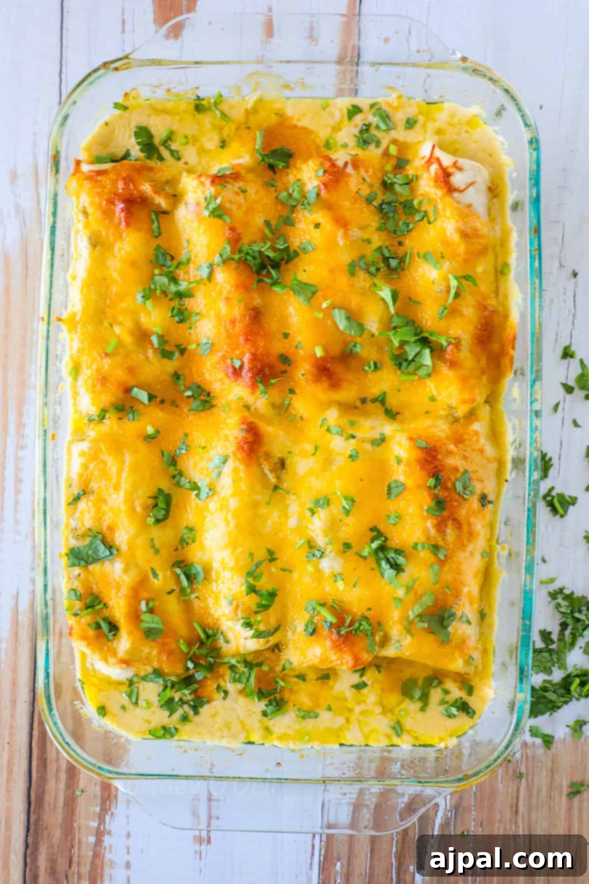 Ultimate Creamy White Chicken Enchiladas 10 A glass baking dish filled with baked enchiladas topped with melted cheese and garnished with fresh chopped parsley.