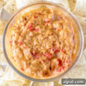 A glass bowl brimming with creamy, spicy smoked chorizo queso, interspersed with diced tomatoes, surrounded by tortilla chips on a platter.