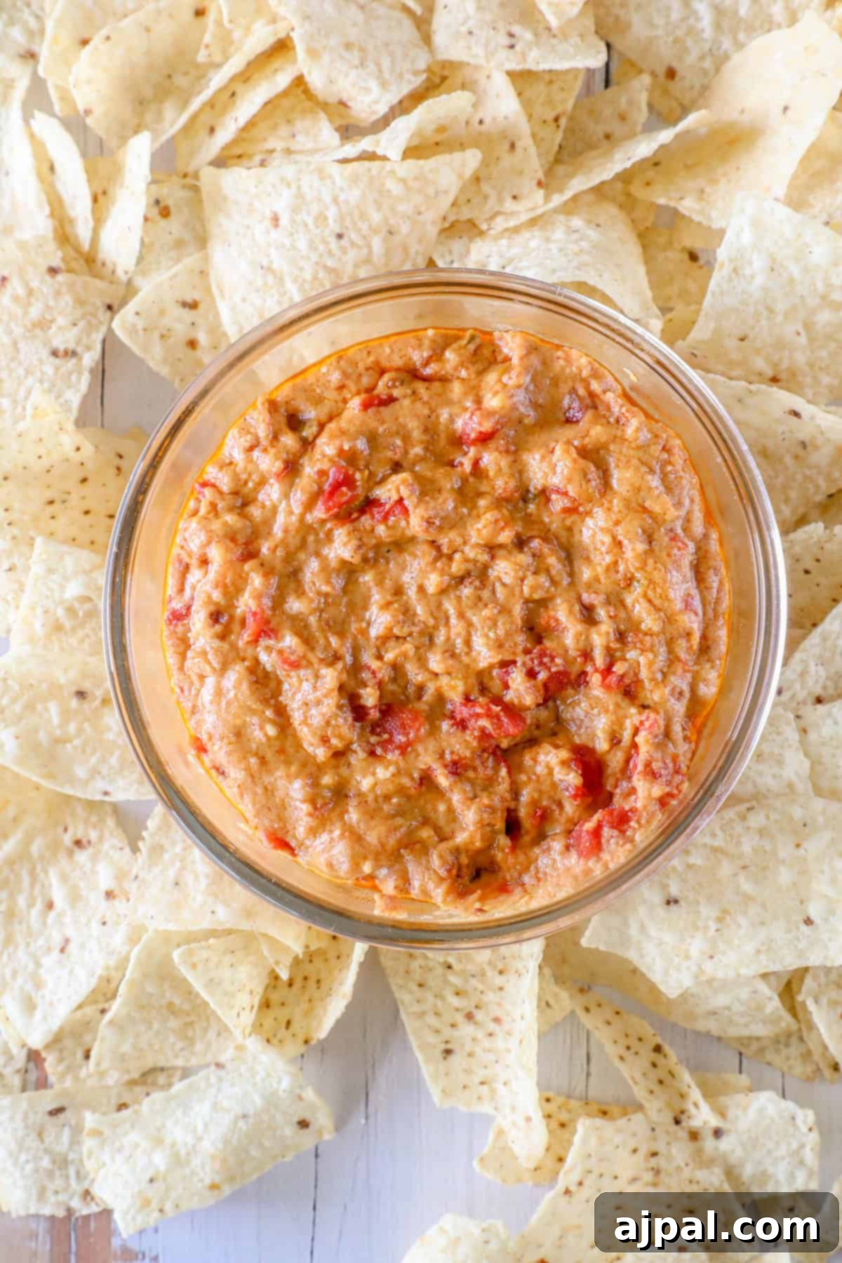Decadent Smoked Chorizo Queso 3 A bowl of creamy red pepper dip, infused with the rich flavors of smoked chorizo queso, surrounded by scattered tortilla chips.